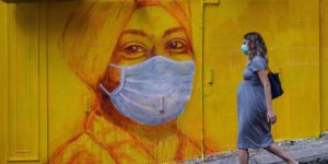 TOPSHOT - A pregnant woman wearing a face mask as a precautionary measure walks past a street mural in Hong Kong, on March 23, 2020, after the citys Chief Executive announced plans to temporarily ban the sale of alcohol in bars and restaurants as a measure to help stop the spread of the COVID-19 caused by the novel coronavirus. - Hong Kong will ban all non-residents from entering the city from midnight on March 24, 2020 in a bid to halt the coronavirus, its leader says, as she unveils plans to stop restaurants and bars serving alcohol. (Photo by ANTHONY WALLACE / AFP)